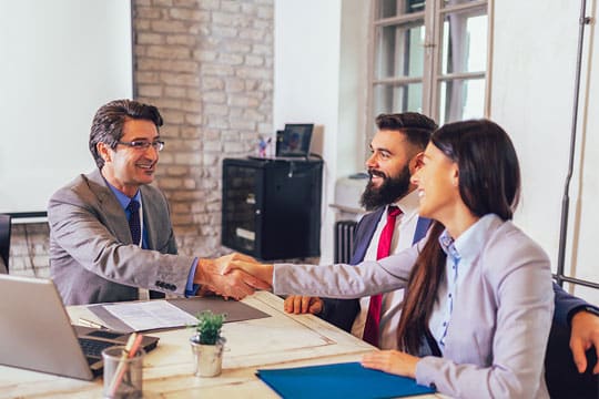 Three people sitting at a table for a meeting. Man shaking a woman's hand